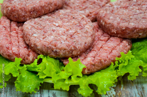 Close-up raw homemade chopped beef burgers on a plate and green salad on wooden table. BBQ preparation, beef products, traditional meat dish. Balanced diet. 