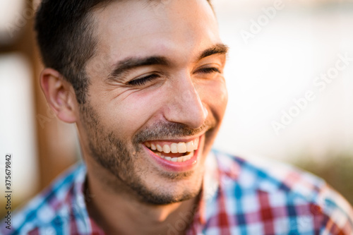 portrait of young laughing man with dark hair in shirt on blurred background.
