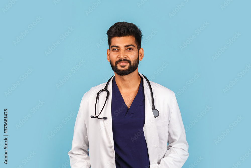 Handsome modern Indian / Asian doctor with stethoscope, in uniform on blue background Handsome modern Indian / Asian doctor with stethoscope, in uniform on blue background