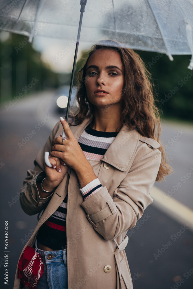 Naklejka premium Portrait of a beautiful young woman with umbrella under the rain at the autumn, outdoors.