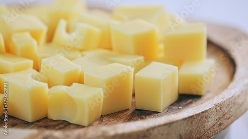 Yellow diced cheese is rotating on a wooden plate. Cubes of cheese photo