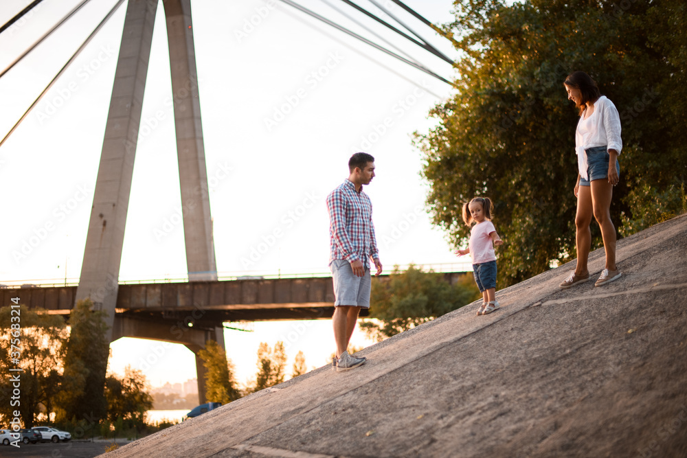 Father and mother walks with little daughter in pink t-shirt on summer day Father and mother walks with little daughter in pink t-shirt on summer day
