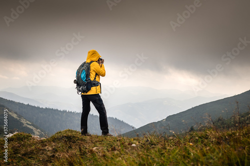 Adventure in nature. Hiker photographing mountain range in bad weather. Woman with backpack hiking outdoors