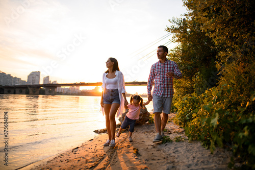Young family couple with child are walking along the sandy river bank