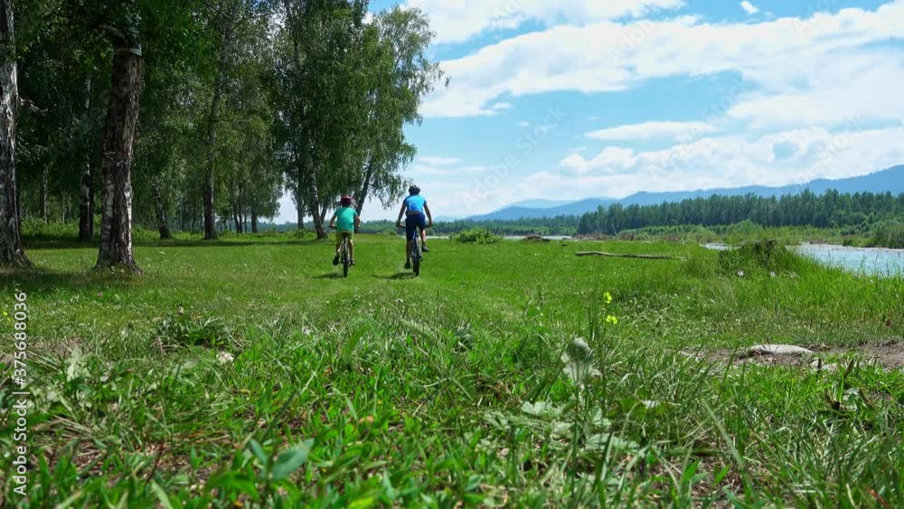 Two young cyclists on mountain bikes ride along the banks of a picturesque mountain river. Two young cyclists on mountain bikes ride along the banks of a picturesque mountain river.