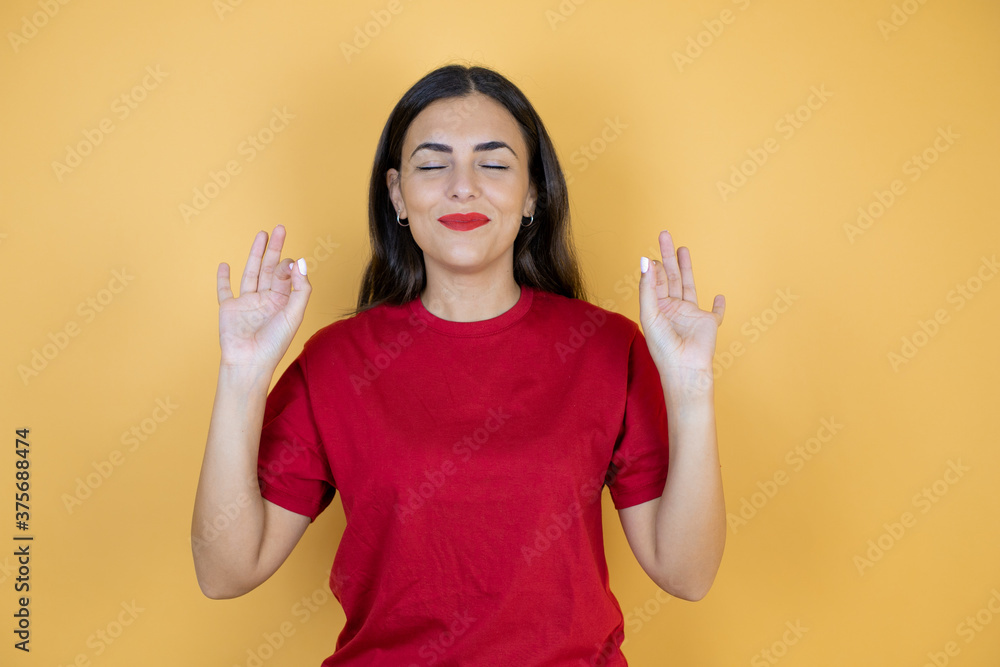 Young beautiful woman over isolated yellow background relax and smiling with eyes closed doing meditation gesture with fingers Young beautiful woman over isolated yellow background relax and smiling with eyes closed doing meditation gesture with fingers