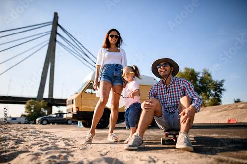 Handsome family couple with small child is resting on the sandy river bank