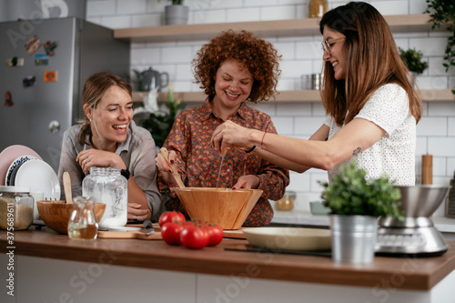 Girlfriends having fun in kitchen. Sisters preparing delicious food at home.