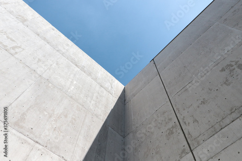Vértice de dos muros de concreto aparente con fondo de cielo azul. Sombra y luz de día. Captura horizontal. 