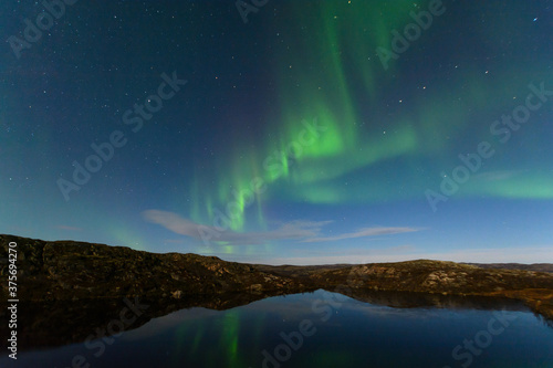 Night sky. Northern lights aurora stars hills reflection in water.