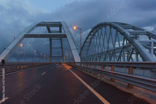 Fototapeta Naklejka Na Ścianę i Meble -  Cars drive under the arches of the Crimean bridge in the late evening. Lights are on
