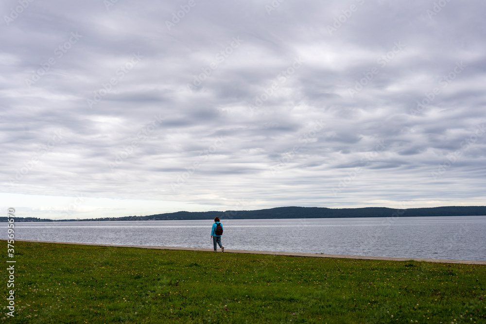 Fototapeta premium woman with orange hair and in a blue jacket resting on the embankment by the lake