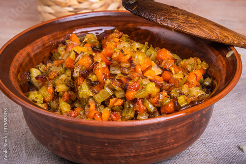 Fried vegetable bases for carrot and celery onion dishes - mirepoix or soffritto in a clay bowl on a wooden table, rustic style, close-up