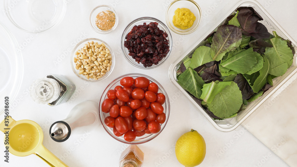 Lettuce salad, cherry tomatoes, dry cranberries, nuts, and ingredients for honey mustard salad dressing close up on kitchen table.