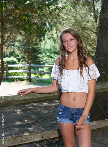 Beautiful girl in an off the shoulder with lace blouse and denim shorts  poses along fence on family farm Stock Photo | Adobe Stock