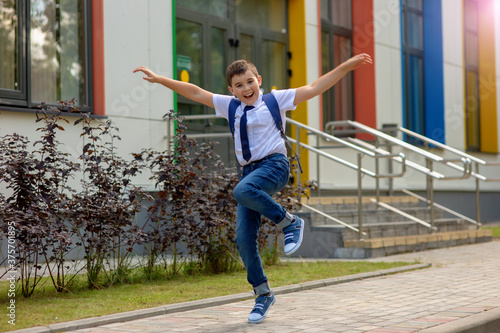 Cheerful fun young schoolboy jumping against school.