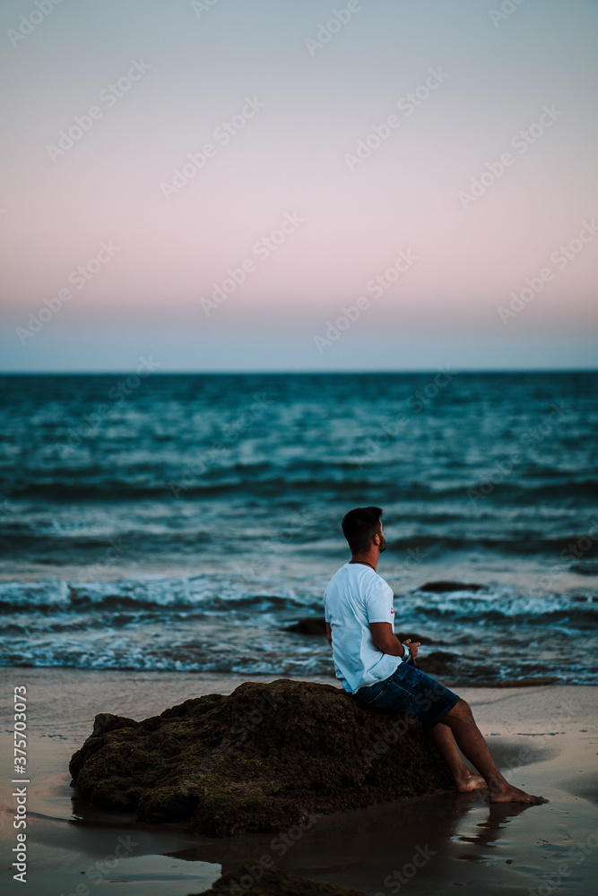 Chico apoyado en al roca mirando al mar
