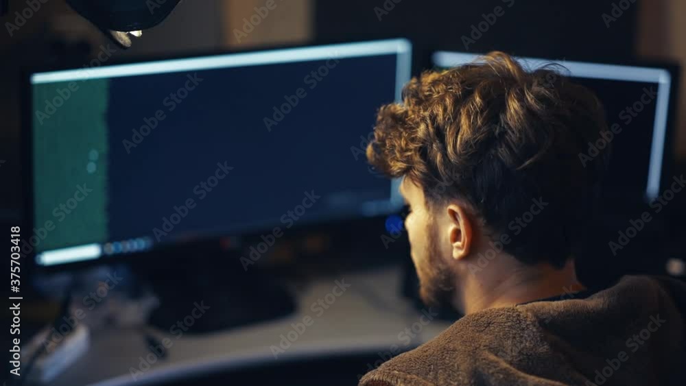 young male programmer hacker works at a computer at home in a terry robe. young male programmer hacker works at a computer at home in a terry robe.