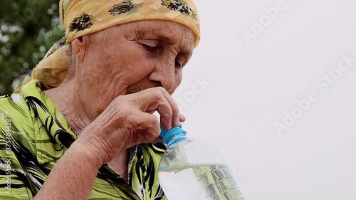 Grandmother drinks water close-up. An old grandmother renews the water balance with pure mineral water close-up. Grandmother with a bottle of water in her hands close-up.