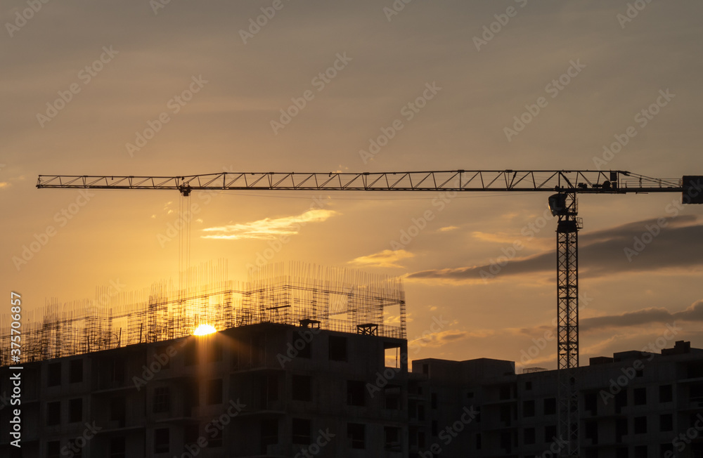 Silhouettes of tower cranes against the evening sky. House under construction. Industrial skyline.