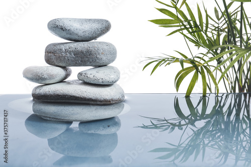 Stack of spa stones and tropical branches in water on white background