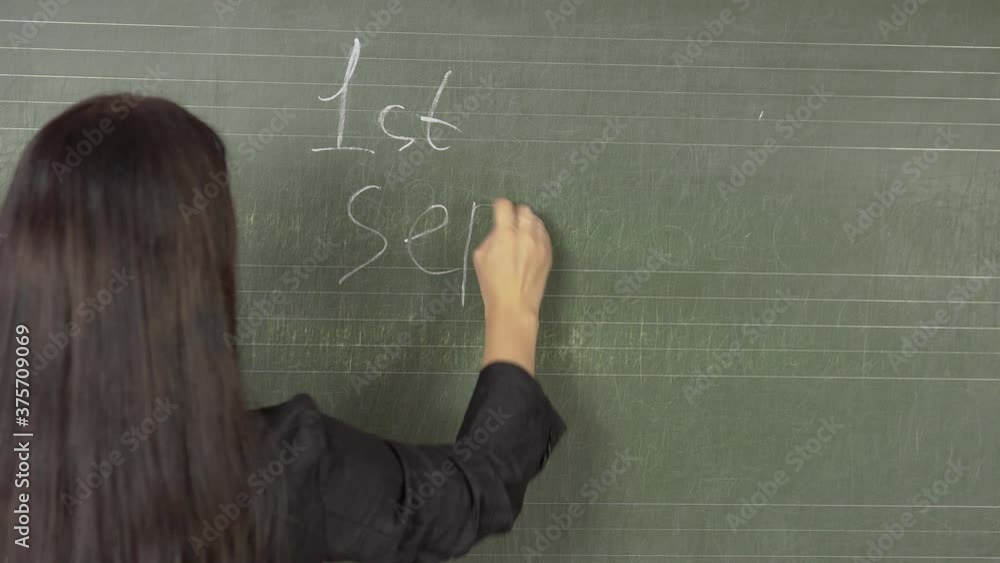 Young brunette teacher writes on the blackboard with chalk on 1st September .4k Young brunette teacher writes on the blackboard with chalk on 1st September .4k