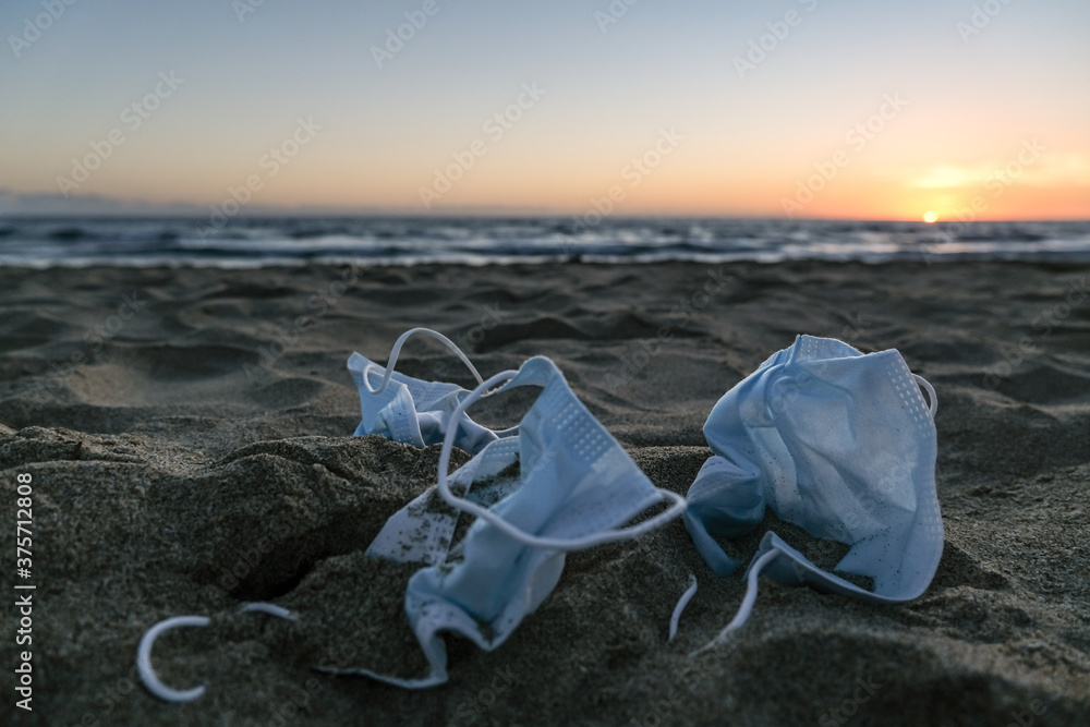 Medical face masks discarded on sea coast over sunset background,covid19 pandemic disease pollution Medical face masks discarded on sea coast over sunset background,covid19 pandemic disease pollution