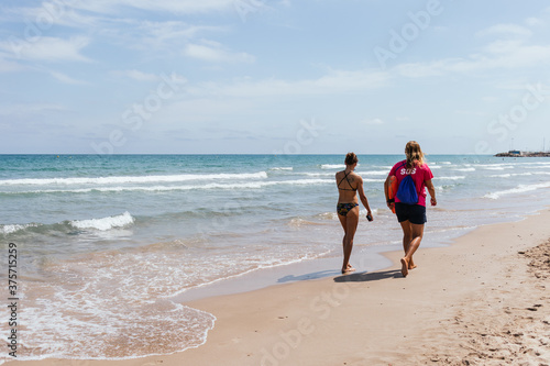 Woman walking along the seashore with a lifeguard on the beach of the Mediterranean Sea with blue sky.