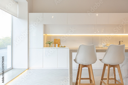 luxury interior design of modern trendy snow white kitchen in minimalistic style with island and two bar stools. huge windows to the floor and a glass rack for dishes