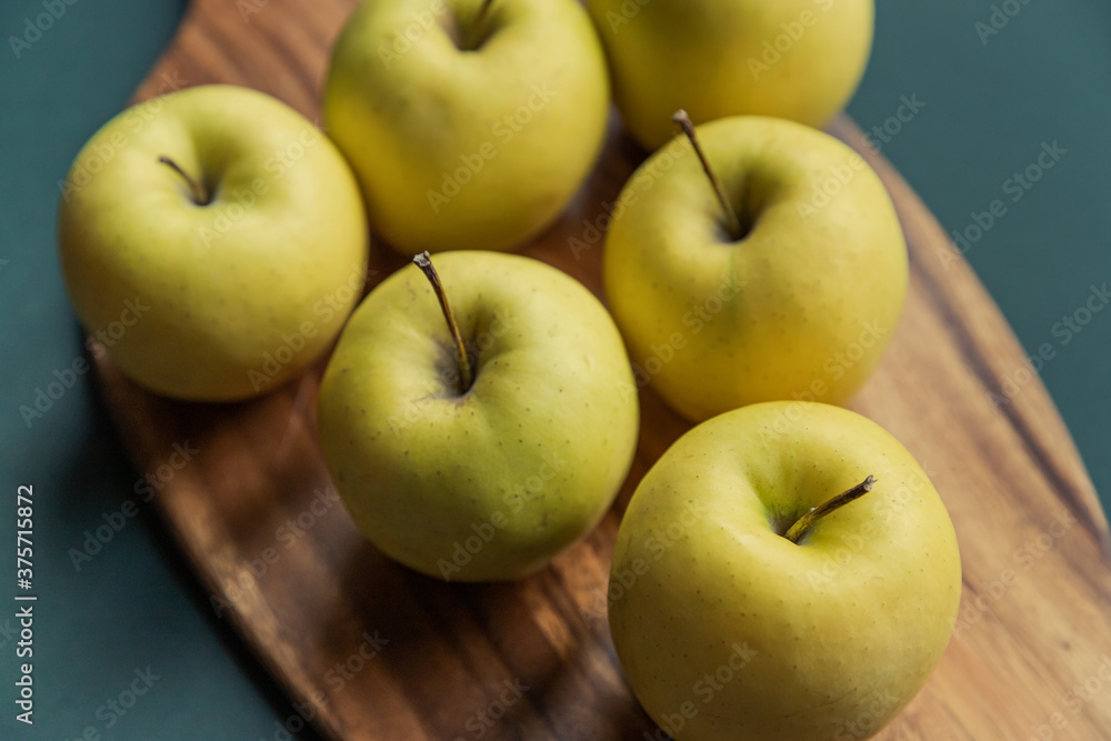 yellow golden delicious apples on green table, wooden cutting board yellow golden delicious apples on green table, wooden cutting board
