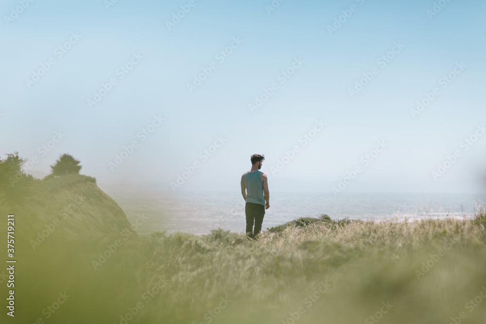 Strong brunette man stands overlooking the pacific ocean on a cliff Strong brunette man stands overlooking the pacific ocean on a cliff