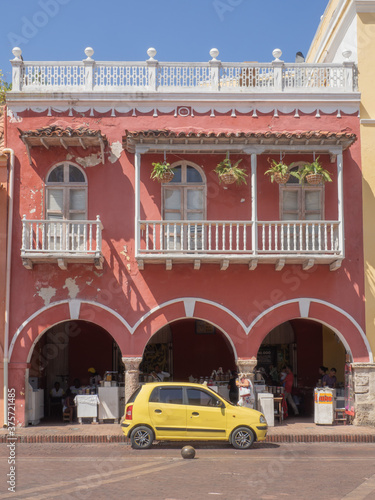 Typical traditional local colorful pastel pink house with  yellow car, taxi, in Cartagena de Indias in Colombia, travel photo