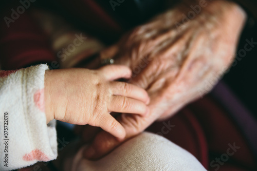 Closeup of the hand of a baby on top of the hand of a senior woman- Family moment of great grandmother and great granddaughter