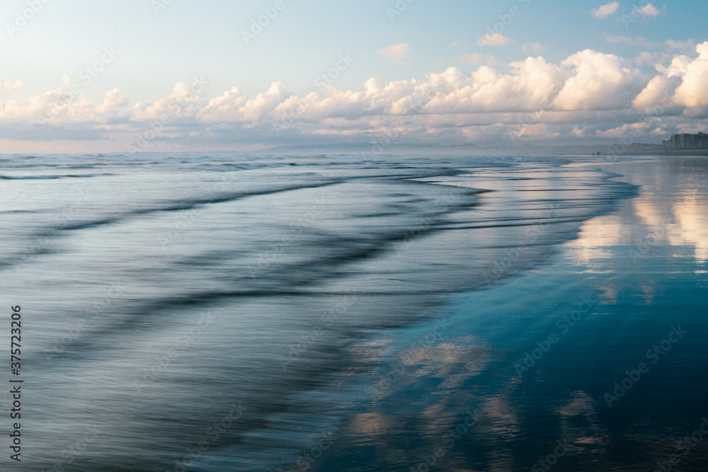 Coastline at sunset with gentle, smooth waves and clouds Coastline at sunset with gentle, smooth waves and clouds