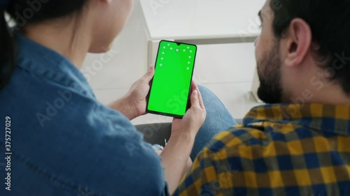 Young couple using cell phone with green screen for internet and social media. Man and woman holding smartphone with green monitor for website. Husband and wife watching video on mobile telephone