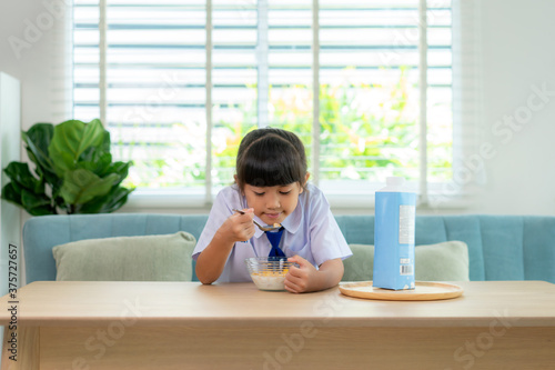 Asian elementary school student girl in uniform eating breakfast cereals with milk in morning school routine for day in life getting ready for school.