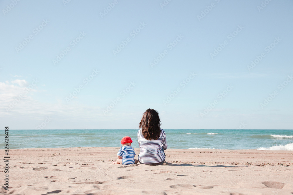 Mom with her baby sitting backward on the beach