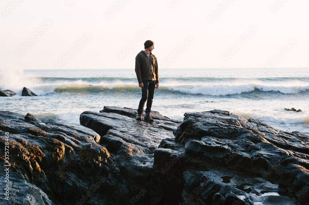 Man standing on rocks looking out to sea at sunset Man standing on rocks looking out to sea at sunset