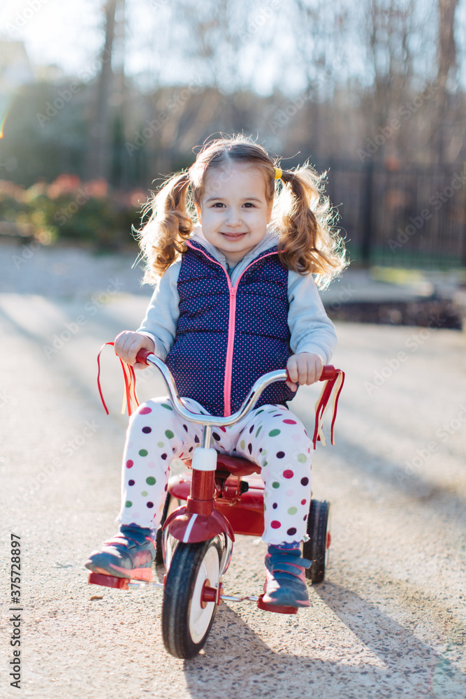 Adorable young girl with pigtails sitting on a tricycle Adorable young girl with pigtails sitting on a tricycle