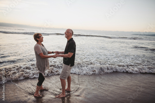 Happy middle aged, retired couple laughing together on ocean beach photo