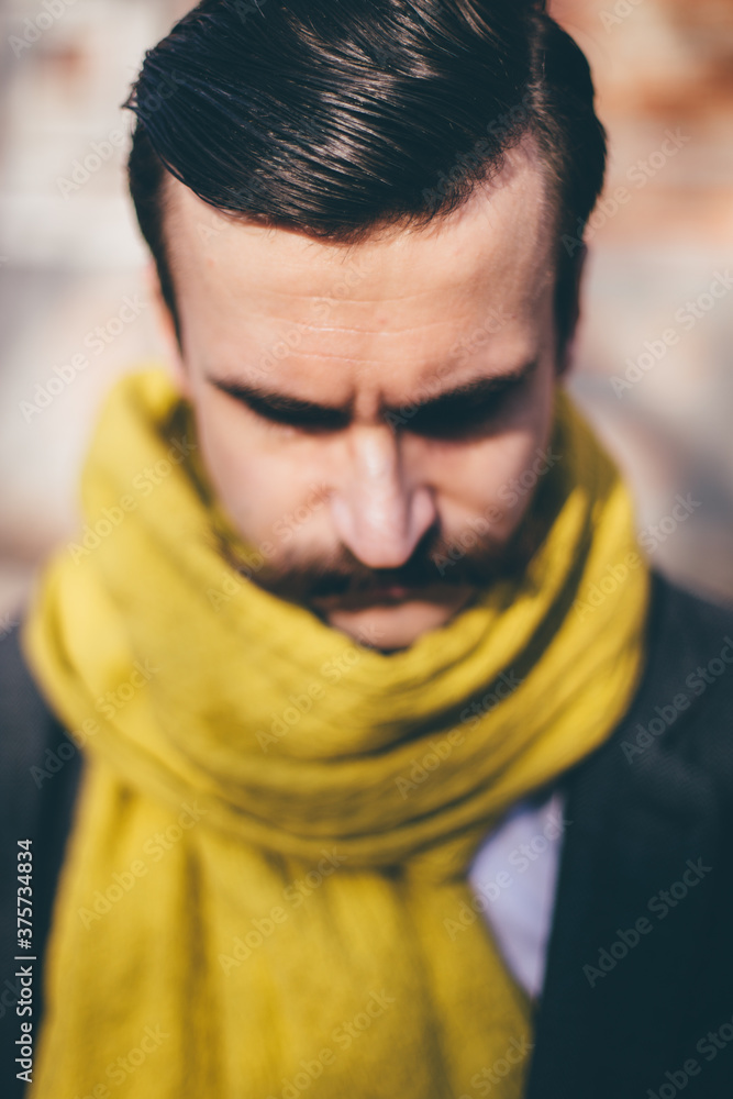 Portrait of mustached men dressed in coat and yellow scarf looking down Portrait of mustached men dressed in coat and yellow scarf looking down