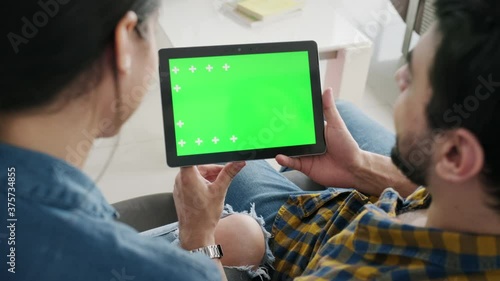 Young couple using tablet with green screen for internet and social media. Man and woman holding monitor with green monitor for website. Friends watching funny film on computer and laughing