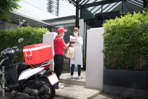 Asian delivery man wearing face mask and gloves in red uniform delivering bag of food and drink to recipient during COVID-19 outbreak