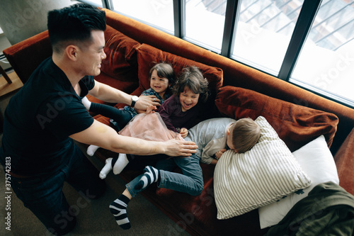 Young father having fun playing with three kids inside - tickling on couch photo