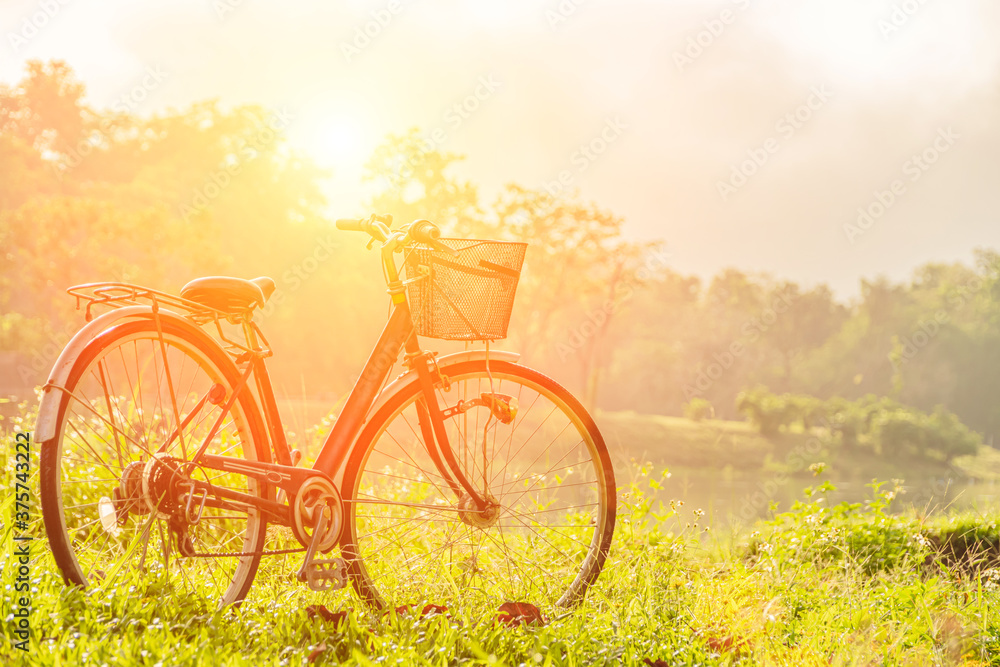 Obraz premium Smooth and beautiful scenery with a bike as the sun rises over the horizon. Vintage style light effect The gentle focus of the bicycle parked in the meadow by the pond. Retro concept.