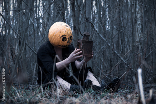 Lost in the woods a guy in a pumpkin with a lantern with a candle wanders in search of a means of getting rid of the autumn depression