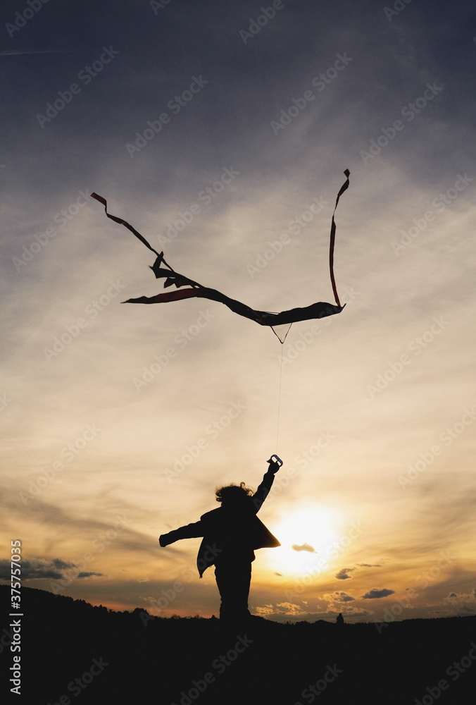 Silhouette of child running with a kite towards the sunset Silhouette of child running with a kite towards the sunset