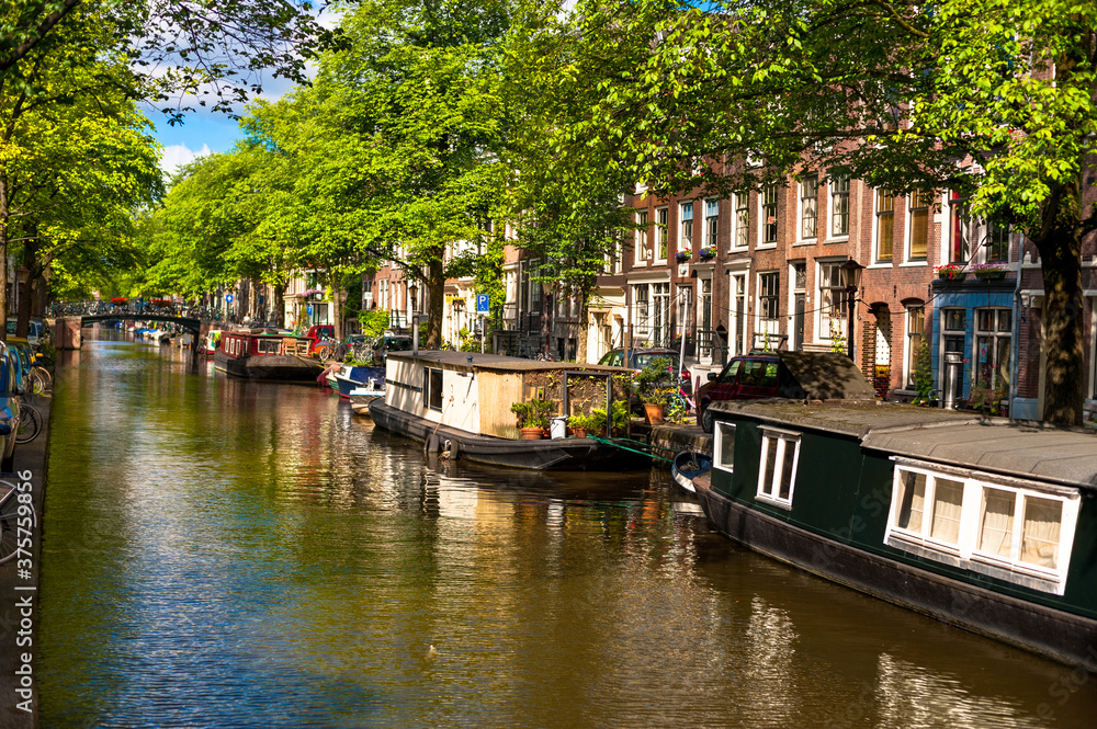 Φωτογραφία Houseboats on Amsterdam Canal with houses in background under beautiful blue, summer sky
