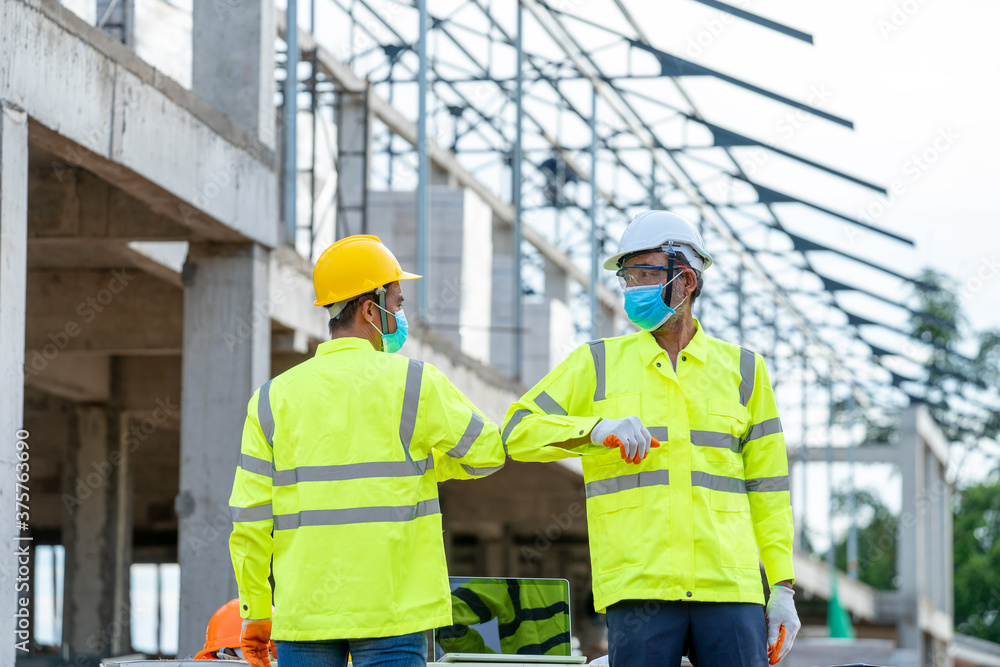 Construction Worker greeting with elbows while wearing protective face masks in building construction site during coronavirus epidemic. Construction Worker greeting with elbows while wearing protective face masks in building construction site during coronavirus epidemic.