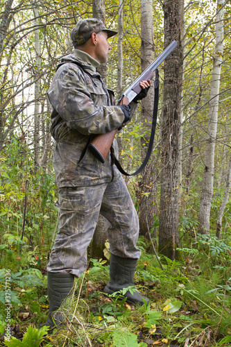 a hunter with a weapon in his hands stands in a thicket of aspen
